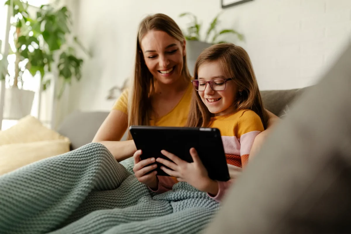 une jeune femme et une petite fille sous un plaid regardant une tablette