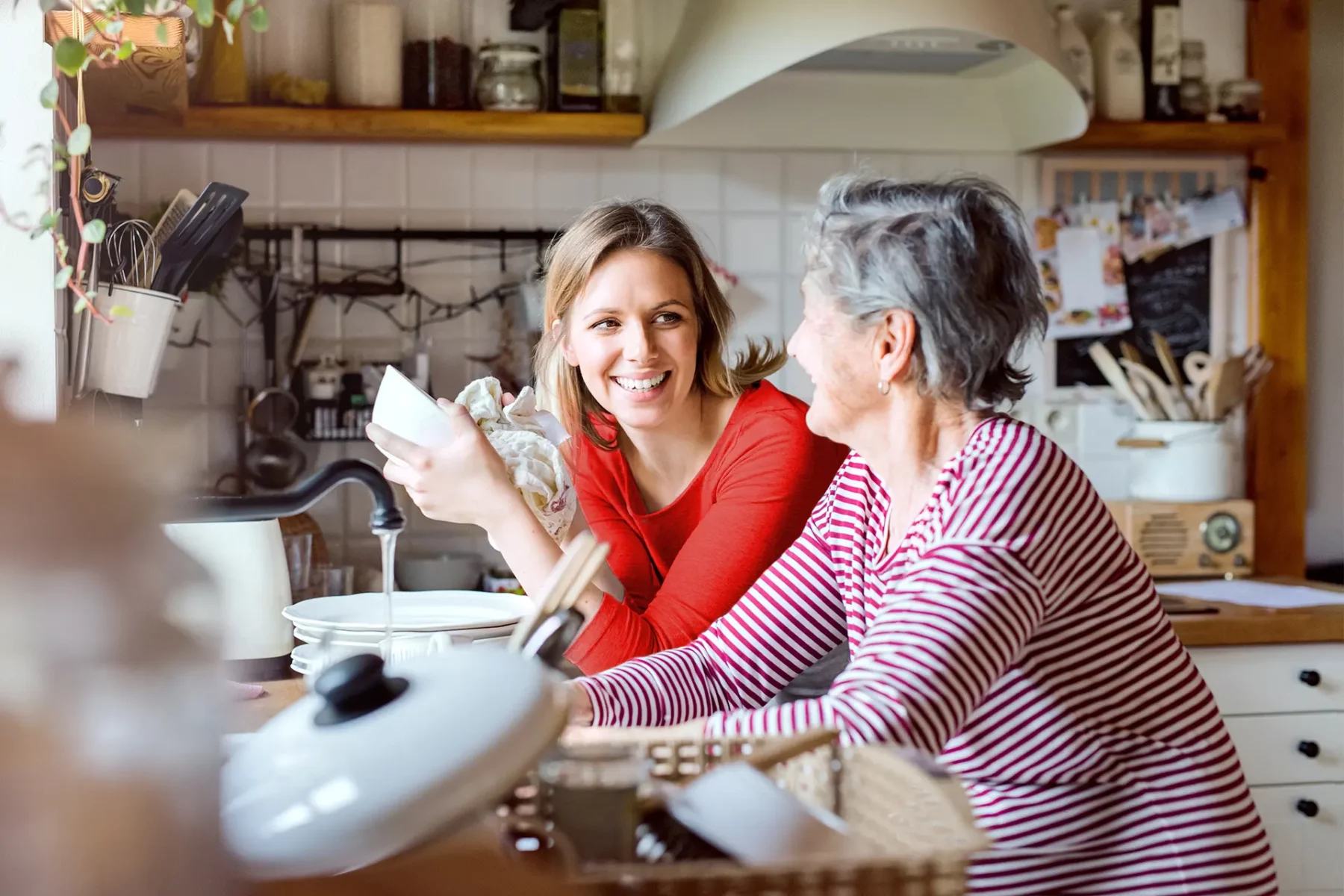 Jeune femme faisant la vaisselle discutant avec une femme âgée