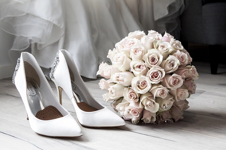 Chaussure de mariée en cuir blanc avec un bouquet de fleur posé à côté