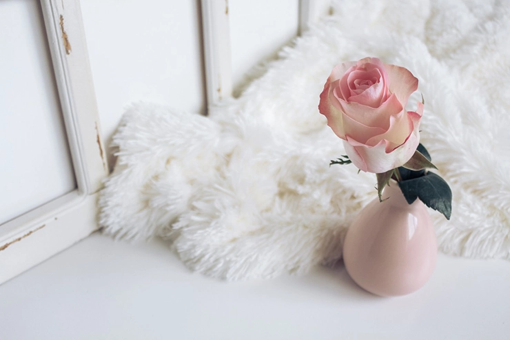 Tapis blanc à poils long posé sur le sol avec une rose dans un vase sur le côté